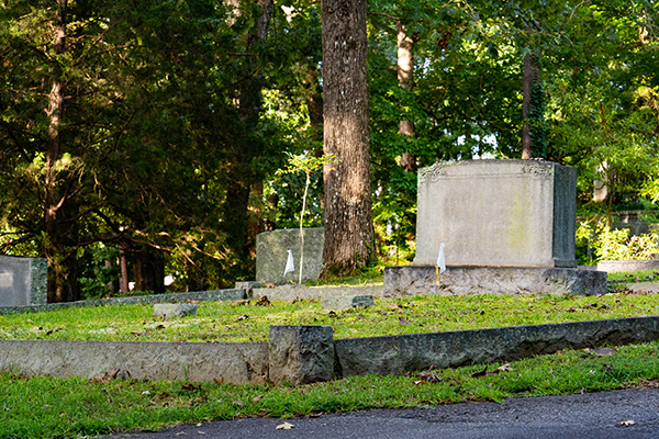 White flags denoting unmarked graves sit in plot with a headstone at Woodland Cemetery.