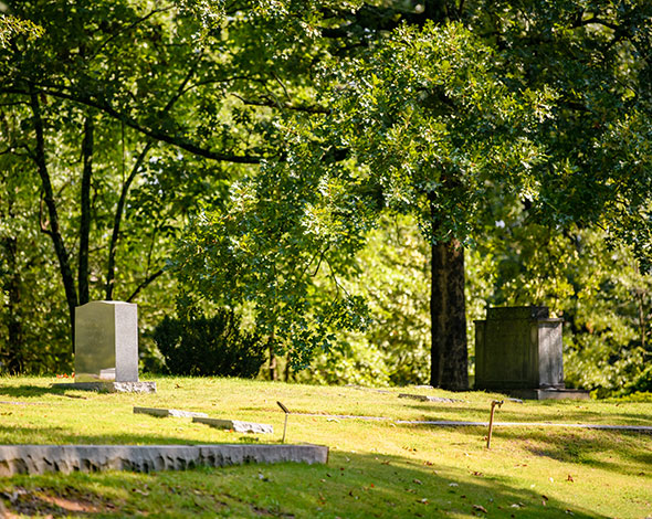 Path around Woodland cemetery with trees on the right and grave markers on the left.