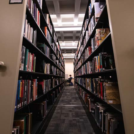 stacks of books frame a student sitting at a desk in the cooper library