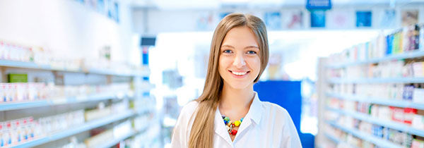 A young woman in a white coat stands in a pharmacy