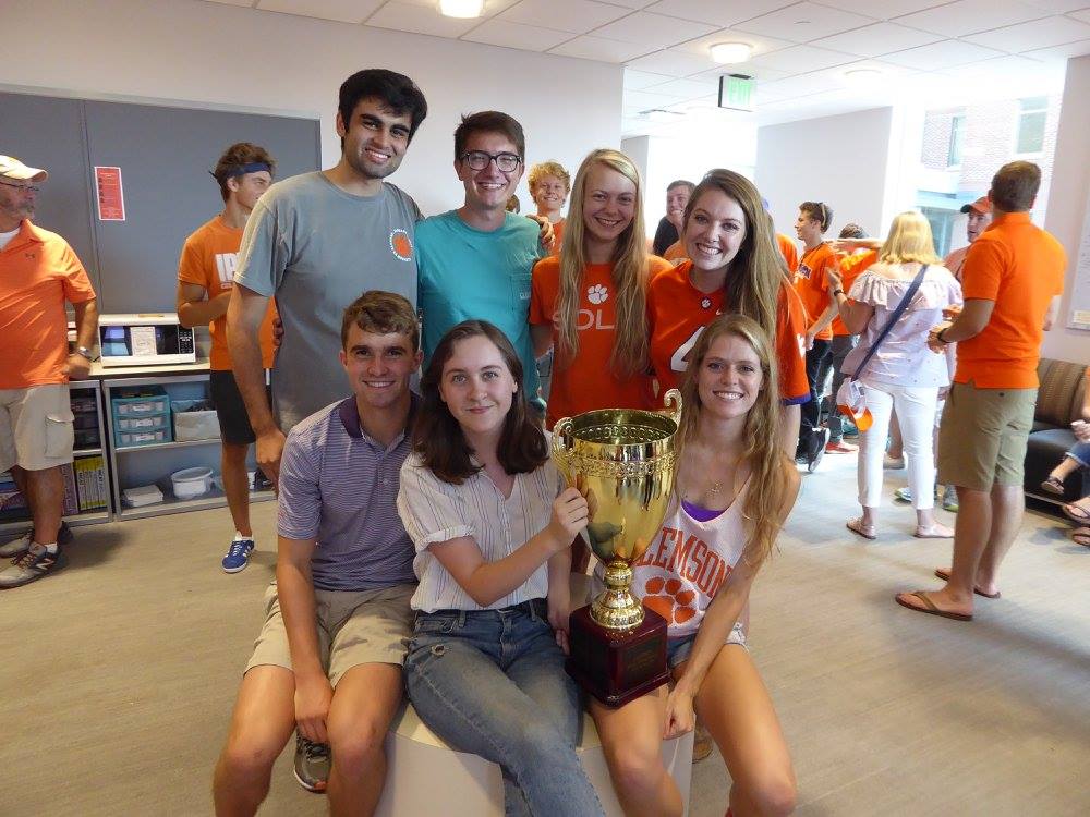 A group of students standing in a classroom holding a trophy cup with pride.