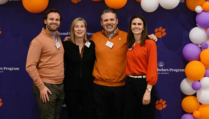 Three NSP alumni posing with former director Jamie Williams (2nd from right) in front of an NSP backdrop.