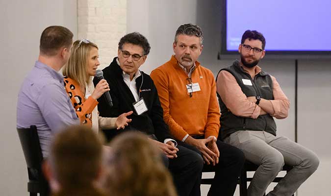 Former NSP directors sitting in chairs as part of a panel. Dean Winslow is speaking into a microphone. 