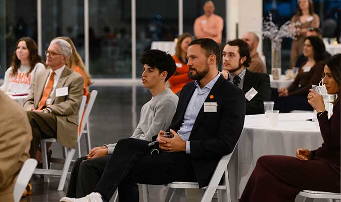 NSP alumnus Joseph Godsey sitting with his son at the celebration, surrounded by NSP alumni and friends. 
