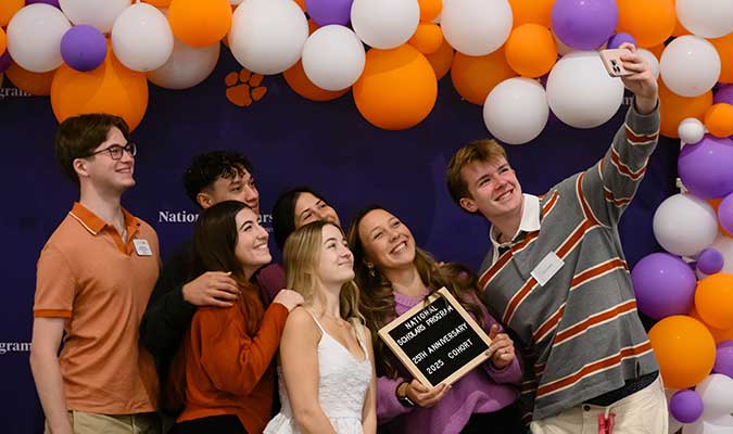 The 2025 cohort of National Scholars posing together for a selfie in front of the NSP backdrop. 