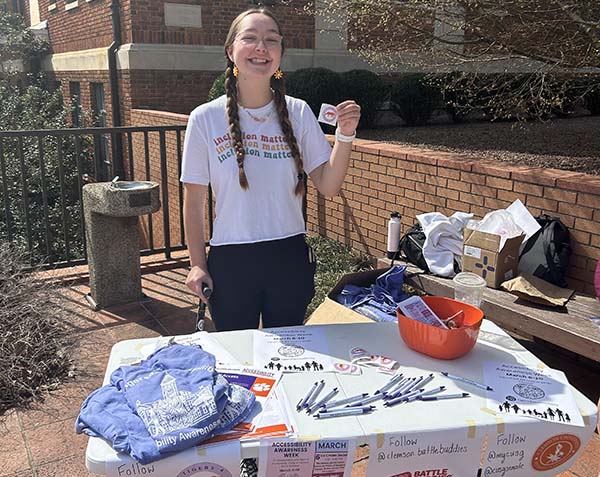 National Scholar Elizabeth Caldwell posing in front of an information table promoting accessibility awareness. 