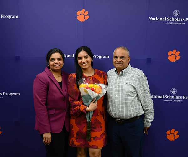 A National Scholar posing with her parents in front of a program backdrop.