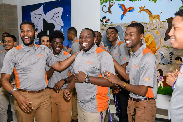 Tiger Alliance students and mentors wearing matching grey and orange buttoned shirts smile and talk during an event. 