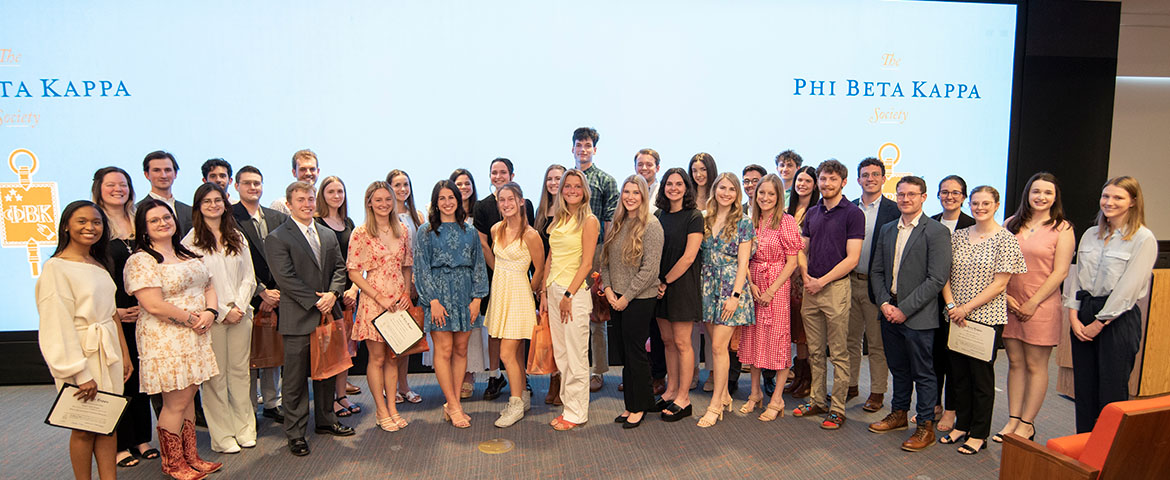 Phi Beta Kappa induction group pose in front of a large screen at the Watt Center