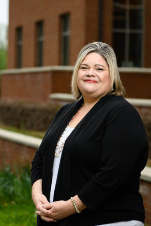 A blond woman in a black cardigan poses outside a brick building.