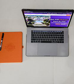 Laptop displaying the Clemson website with an orange notebook to the left.