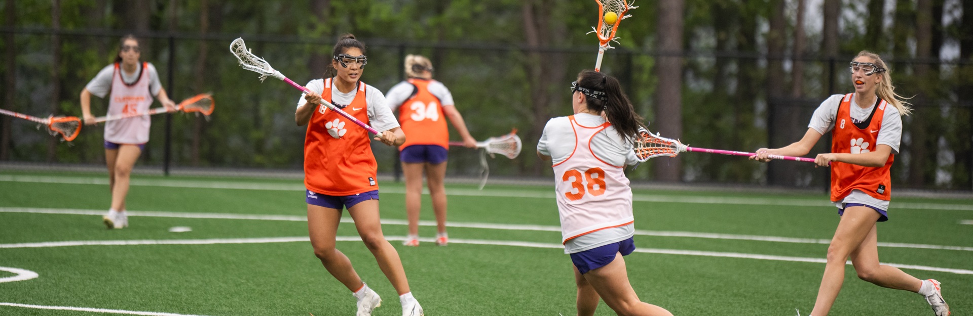 Lacrosse players participating in a scrimmage match on a green field.