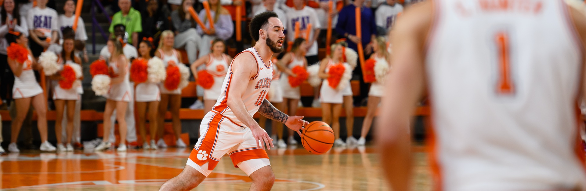 Clemson basketball players dribbling the ball down the court. Cheerleaders can be seen in the background.