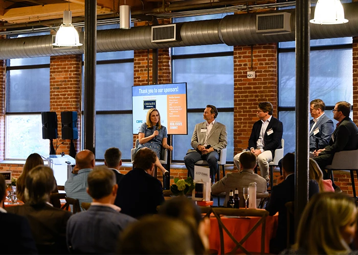 A group of five panelists present to a crowd of people dining inside a brick building.