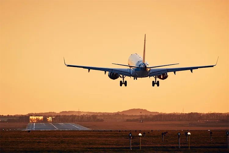 A plane takes off into the orange sky.