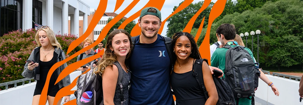 A male student and two female students with their arms around each other smiling with an orange tiger stripe graphic overlay in the background.