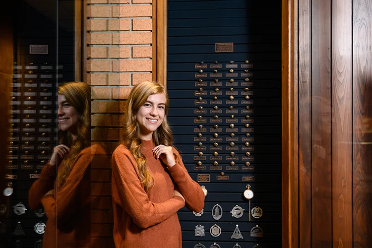 A female student stands in front of a Clemson Ring display case that holds several rings from over the years.