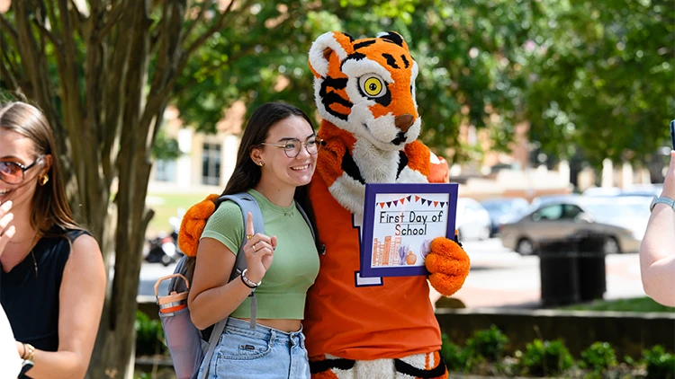 A female student poses with the tiger mascot holding up a sign reading first day of school