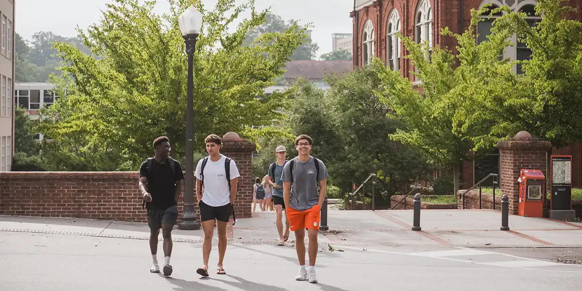 Three young men casually walking together across campus, smiling and engaged in conversation.