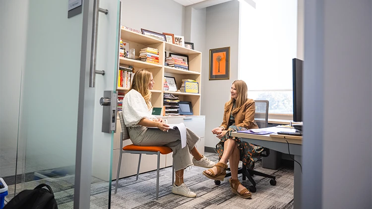 A female student and faculty member sit in an office talking to one another