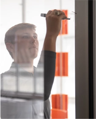 A male student writes a math equation on a glass wall.