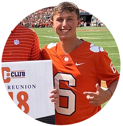 A male student wears an orange football jersey with the number six written as a figure in white.