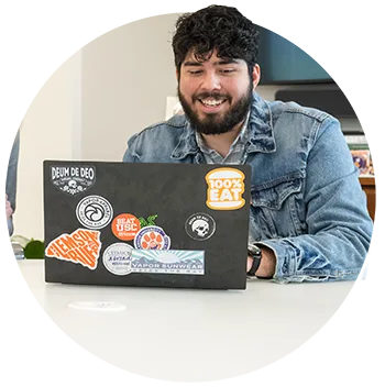 A male student wearing a denim jacket sits at a desk in front of his laptop.