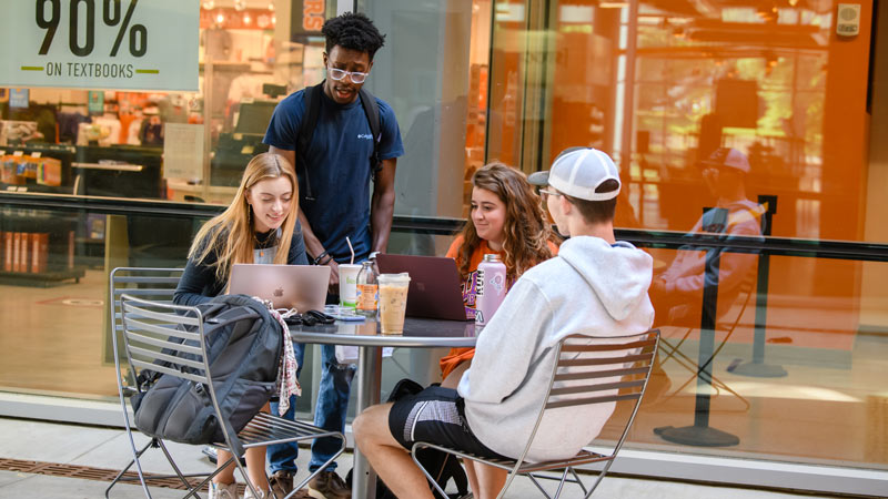 Students socialize around an outdoor table on their laptops