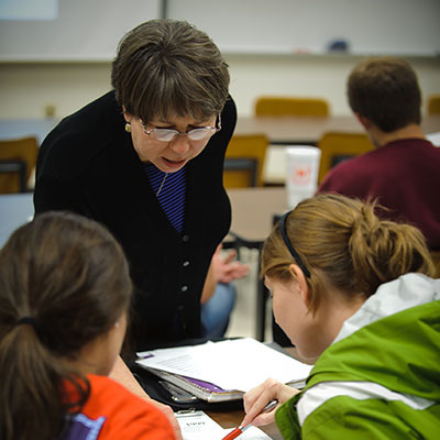 Faculty member leans over to review work being done by two students.