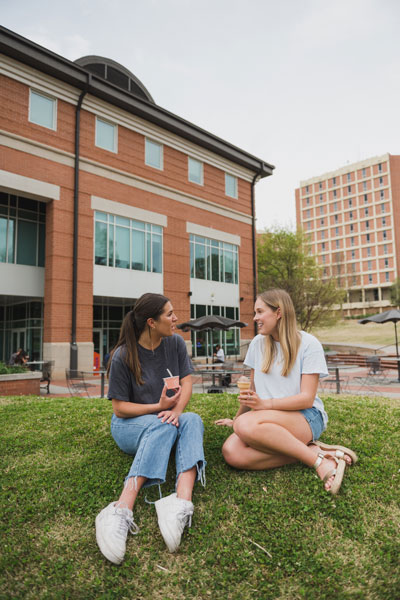 Two female students eat Ice Cream on a grassy lawn in front of the Hendrix Student Center