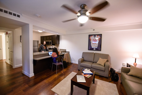 two female students sit at the bar in the kitchen of a lightsey bridge apartment with the furnished living area in the foreground
