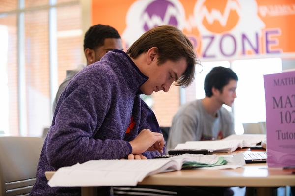 a male student studies a text book with a sign for tutoring in the background