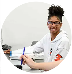 A female Bridge student wearing a grey clemson sweatshirt works at a computer with another student.