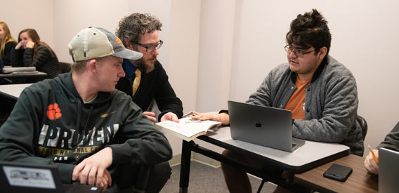 an instructor talks in class with two male students at desks