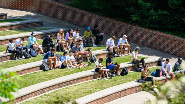 students study and socialize filling the brick seating of the amphitheater on a sunny spring day