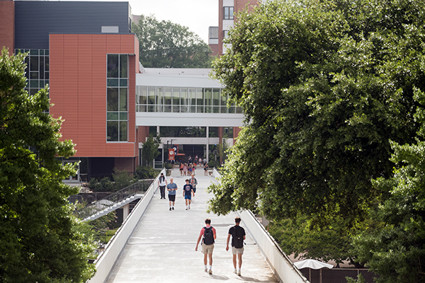 Multiple students walking across the cement bridge with Clemson campus classromm building in the background.