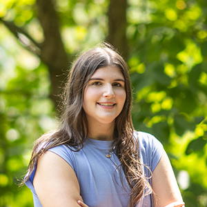 Phoebe Beard standing outside with trees and green leaves in the background.
