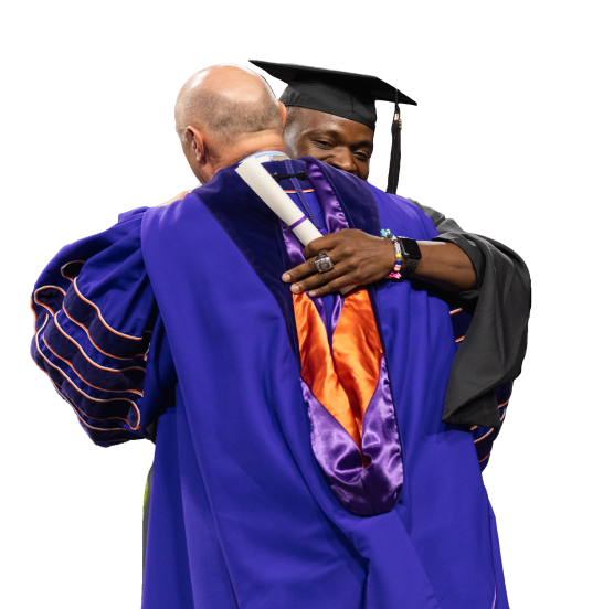 President Clements hugs a smiling graduate as he accepts his diploma.