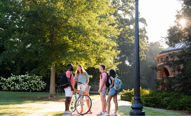 Four students stand talking and smiling.