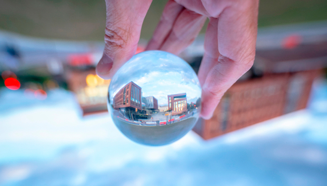 Hand holding glass ball the reflects the new Wilbur O. and Ann Powers College of Business building.