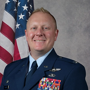 Portrait of a military officer in uniform, standing in front of an American flag, showcasing their medals.