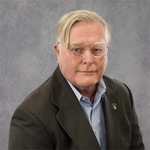 Professional portrait of a middle-aged man wearing glasses and a suit jacket, with a neutral gray background.