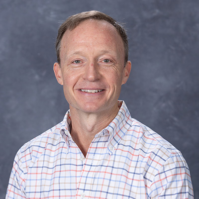 Smiling portrait of a man in a checkered shirt on a gray background.