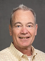 Professional headshot of a smiling man with short gray hair and a plaid shirt.