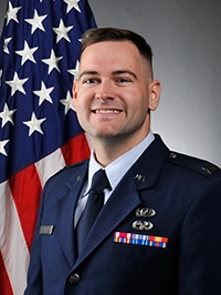 Portrait of a uniformed military service member smiling in front of an American flag.