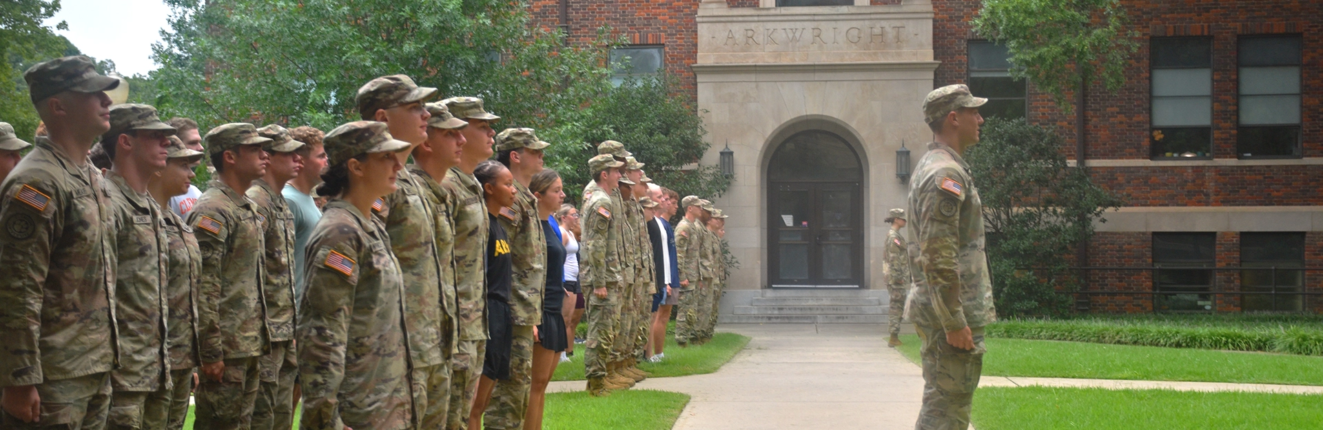 Cadets in camouflage marching in parade with Clemson flag.