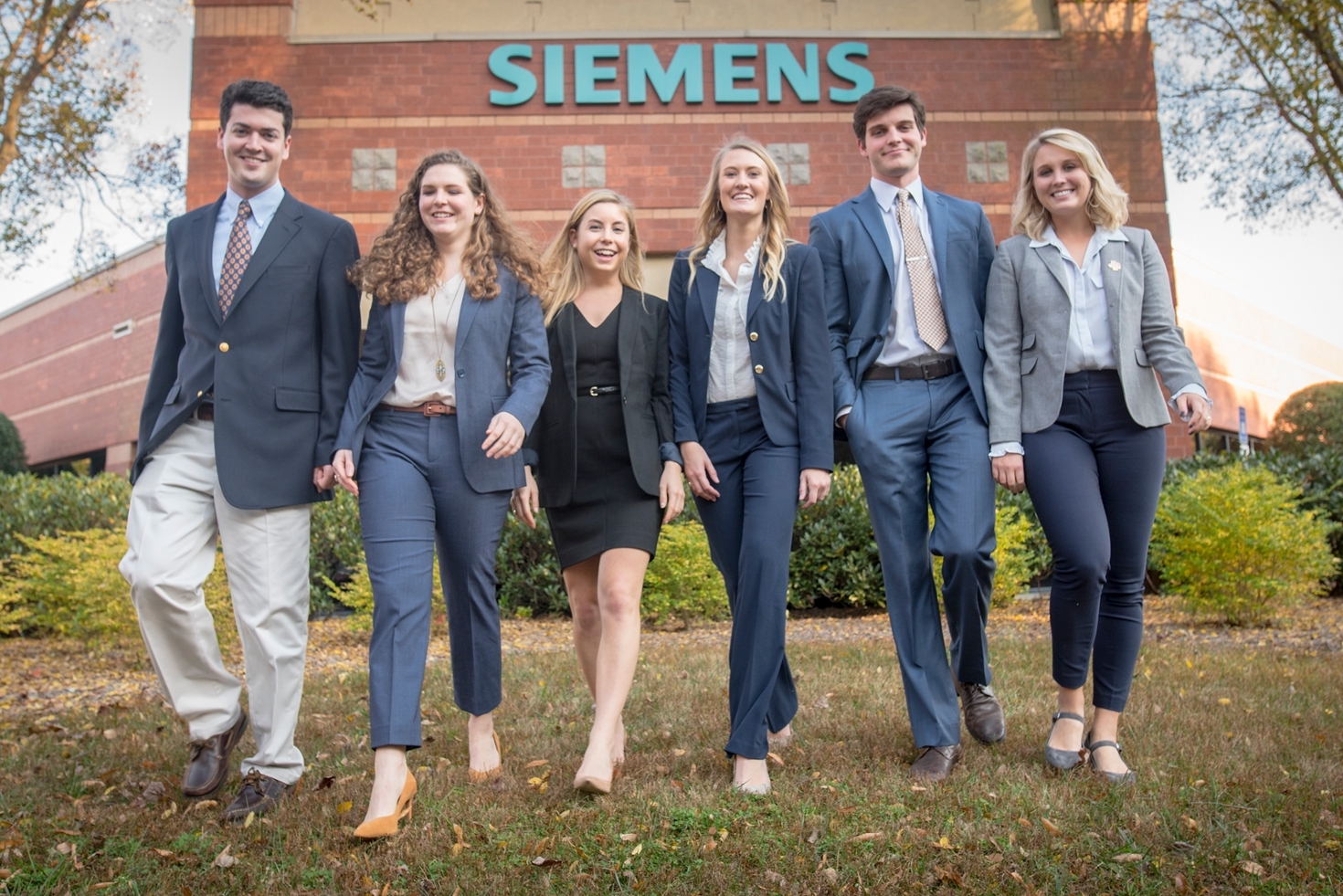 Four female and two male students walking side by side downhill in front of Siemens building.