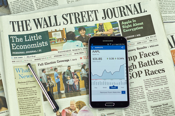 Wall Street Journal newspaper with cell phone and stylus laying on top of newspaper.