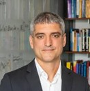 Professional headshot of a man with gray hair, wearing a black suit.