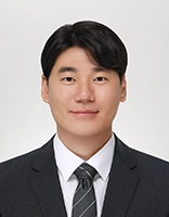 Professional headshot of a man in a suit and tie, featuring a friendly expression against a plain background.